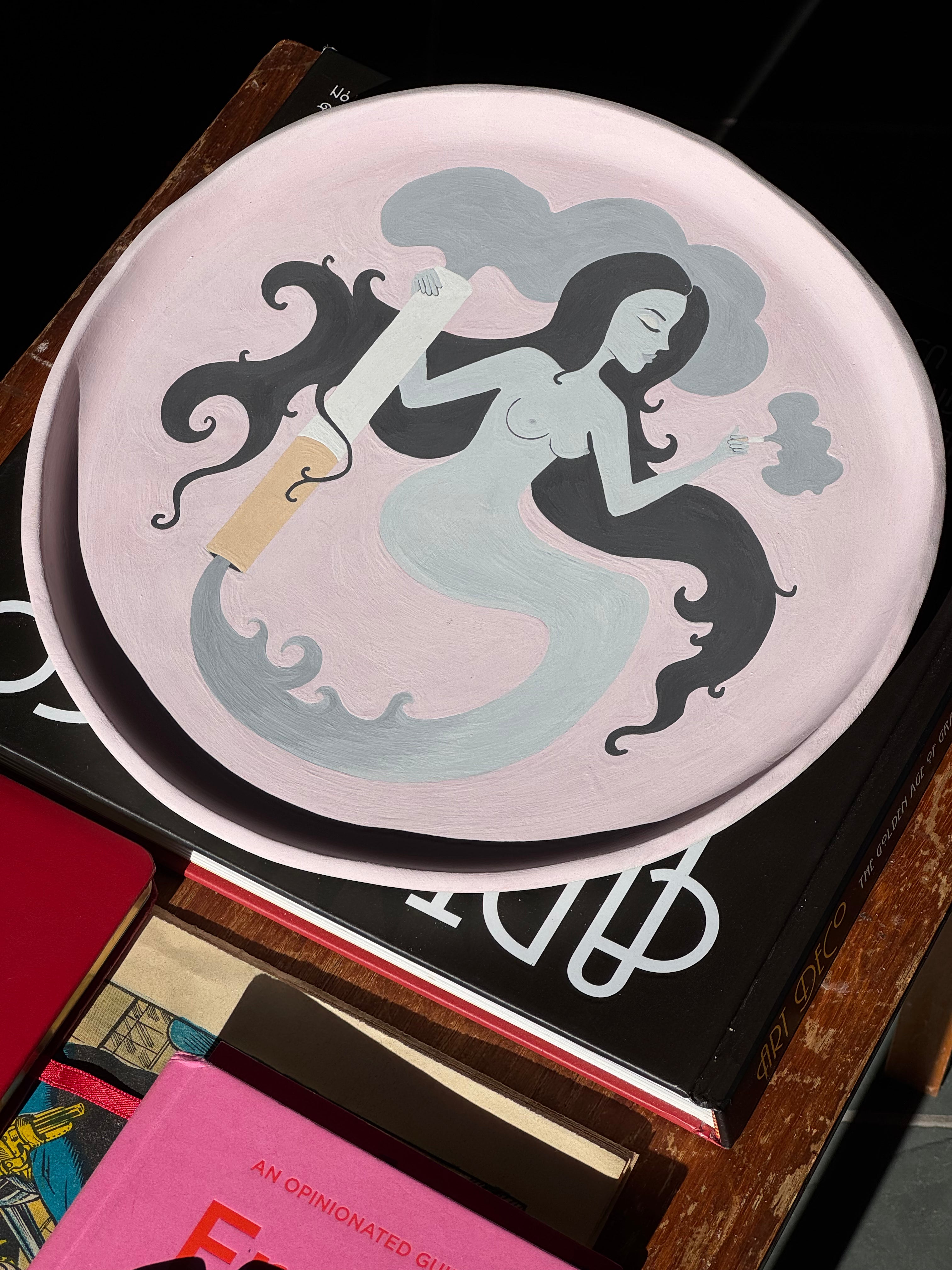A curation of coffee table books, and a baby pink, hand-painted, ceramic tray on an old wooden surface.
