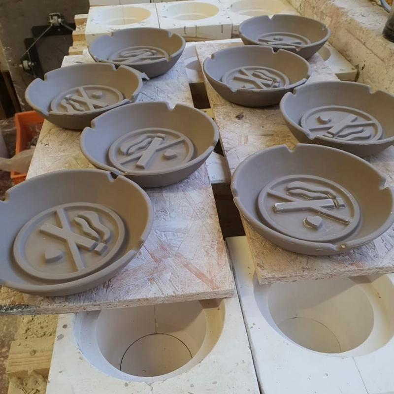 Several round gray ceramic bowls or plates with embossed symbols, arranged on white ceramic blocks in a workshop setting.