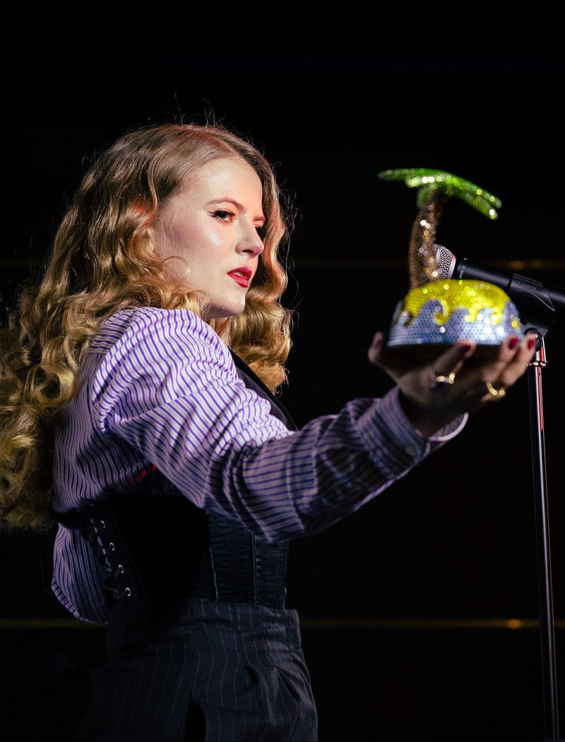 Miss Jessica Booty holding the sparkling Paradise Island ceramic sculpture with a microphone at the Karma Cabaret.